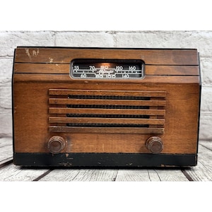 May include: A vintage Majestic radio with a wooden cabinet. The radio features a tuning dial, speaker grill, and two knobs. The cabinet is brown with black accents, showing signs of wear. The radio's dial displays the Majestic brand name.