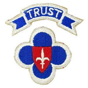 May include: A blue and red military patch with a white border and the text "TRUST" on a blue ribbon above it.