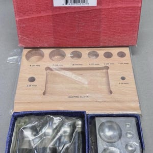 May include: A jewelry-making dapping set with a wooden dapping block, punches, and a metal forming block. The wooden block has various sized circular indentations. The set is packaged in a red box and blue boxes.