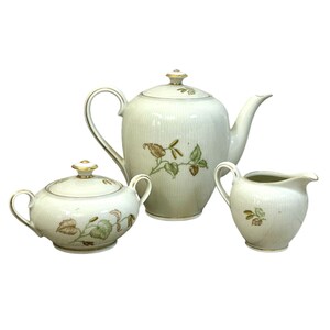 May include: A white porcelain tea set with a floral design. The set includes a teapot, creamer, and sugar bowl.
