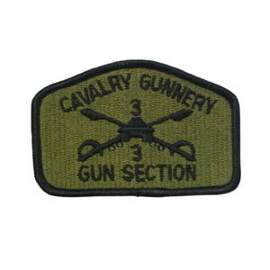 May include: A green and black embroidered patch with the text "Cavalry Gunnery 3 Gun Section". The patch features a crossed pair of machine guns with a helmet and the number "3" on top.