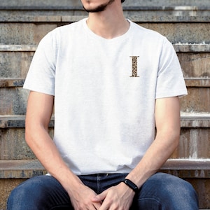 Pode incluir: Uma camiseta cinza claro com a letra "I" estampada em padr&atilde;o de leopardo no peito esquerdo. A camiseta tem mangas curtas e gola redonda. A pessoa est&aacute; usando jeans azuis e um rel&oacute;gio preto.