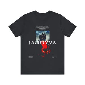 Puede incluir: Camiseta negra con un diseño gráfico que presenta una casa embrujada, la palabra "LACHRYMA" y el texto "IN THE MIDDLE OF THE NIGHT IT FEEDS..." en blanco. El diseño incluye acentos rojos y naranjas.