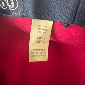 Peut inclure: Gros plan d'un chapeau en laine rouge avec un bord bleu fonc&eacute;. Une &eacute;tiquette indique "WPL 5923 100% Laine/Lana/Laine" et "LARGE". L'&eacute;tiquette indique &eacute;galement "Made in U.S.A."