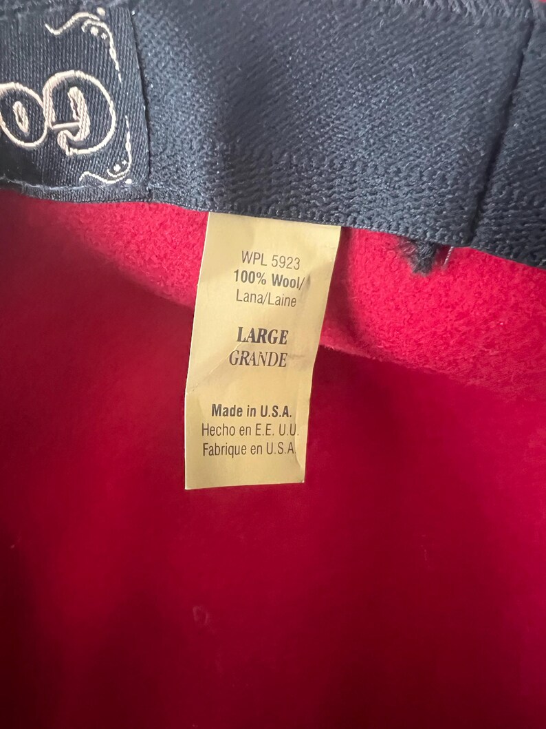Peut inclure: Gros plan d'un chapeau en laine rouge avec un bord bleu fonc&eacute;. Une &eacute;tiquette indique "WPL 5923 100% Laine/Lana/Laine" et "LARGE". L'&eacute;tiquette indique &eacute;galement "Made in U.S.A."