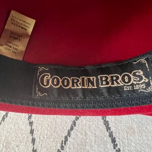 Peut inclure: Gros plan sur un chapeau en laine rouge avec une bande int&eacute;rieure noire. Le chapeau porte une &eacute;tiquette avec le texte "GOORIN BROS. EST. 1895". Le chapeau est &eacute;tiquet&eacute; "LARGE" et fabriqu&eacute; aux &Eacute;tats-Unis.
