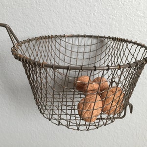 May include: A wire basket with a handle, holding several walnuts. The basket is made of a fine wire mesh and has a rounded shape.