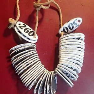 May include: A white and black numbered necklace with a string of round ceramic tags. The tags are numbered from 260 to 300.