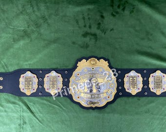 May include: A black leather wrestling championship belt with gold and silver accents. The center plate features the words "Heavyweight Champion" and a design of two wrestlers shaking hands. The belt has multiple side plates with gold and silver accents.