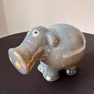 May include: A ceramic hippo figurine with a blue and brown glaze. The hippo has small, round eyes, a large snout, and stubby legs. The figurine is a decorative item.
