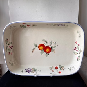 May include: Rectangular serving platter with a cream-colored surface and a light blue border. The platter is decorated with illustrations of red apples, grapes, strawberries, and cherries. The fruit illustrations are accompanied by green leaves and white flowers.