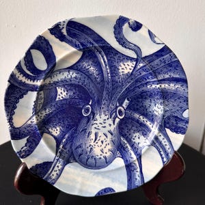 Puede incluir: Un plato de cer&aacute;mica blanco y azul con una ilustraci&oacute;n detallada de un pulpo. El pulpo est&aacute; representado en un tono azul profundo, con intrincado trabajo de l&iacute;neas. El plato tiene una forma ligeramente irregular y org&aacute;nica.