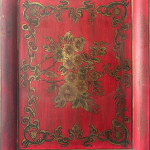 May include: A rectangular red serving tray featuring a central gold floral illustration and a decorative gold border. The tray has integrated handles at the top and bottom edges, with a distressed finish visible along the outer rim and edges.
