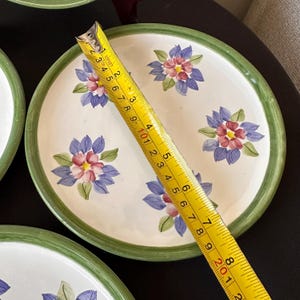 May include: White ceramic plate with a green rim and floral design. The plate features blue and pink flowers. A measuring tape shows the plate is approximately 8 inches in diameter.