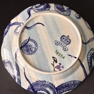 Puede incluir: Plato de cer&aacute;mica blanco y azul con dise&ntilde;o n&aacute;utico. El plato presenta tent&aacute;culos de pulpo azules alrededor del borde y un dise&ntilde;o central con un barco y el texto "ASSOCIATION". El plato tambi&eacute;n tiene el texto "S.H.& Co." y el n&uacute;mero "38354".