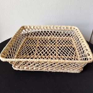 May include: A rectangular woven basket with a lattice design. The basket is made of natural-colored woven material and has a slightly raised edge. The basket is empty and sits on a black surface.