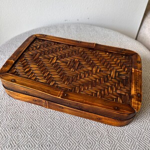 May include: A rectangular bamboo box with a woven top and a dark brown frame. The box is made of natural bamboo and has a warm, inviting appearance. The woven pattern adds texture and visual interest to the design.