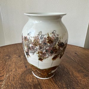 May include: White ceramic vase with a brown, pink, and gray abstract design. The vase has a rounded body and a wide opening.