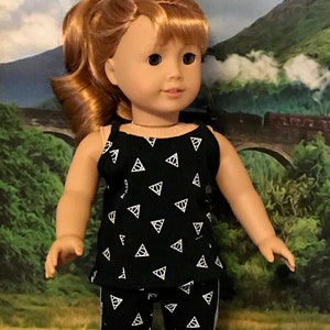 May include: A doll wearing a black pajama set with white triangle symbols. The pajama top is a tank top style, and the pants have a white stripe down the side. The doll has red hair and is standing in front of a landscape.