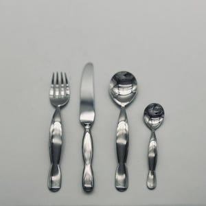 May include: A set of four stainless steel utensils: a fork, a knife, a tablespoon, and a teaspoon. The silverware has a reflective, polished finish and a unique, curved handle design. The arrangement is symmetrical against a neutral background.