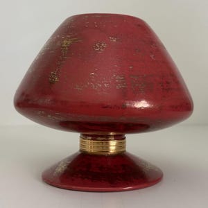 May include: A red ceramic vase with a gold rim and gold flecks throughout. The vase has a wide, flared top and a round base.