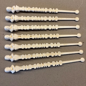 May include: Seven white plastic cocktail stirrers with a small figurine of a man at the top and the words "OLD GRAND-DAD" printed on the side.