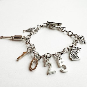 May include: A silver charm bracelet with a variety of charms, including a fish, a screwdriver, the numbers 1025, and a charm with the word "Michigan".