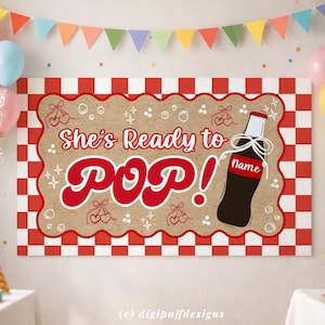 以下が含まれることがあります： 赤と白のチェック柄の縁と茶色の中央部がある長方形の看板。「She's Ready to POP！」と赤い文字で書かれており、ソーダボトルのイラストが描かれています。装飾要素には、さくらんぼと星が含まれています。