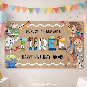 Może przedstawiać: Baner urodzinowy z postaciami z filmu Toy Story. Na banerze widnieje napis "You've Got a Friend Who's THREE Happy Birthday Jacob!" z kolorowymi literami i ilustracjami Woody'ego, Buzza Astrala i innych postaci.