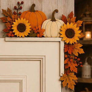 May include: A decorative L-shaped door corner accent featuring a vibrant autumn theme. It displays a large orange pumpkin, a smaller white pumpkin, two bright yellow sunflowers, and an arrangement of orange, red, and brown maple leaves.