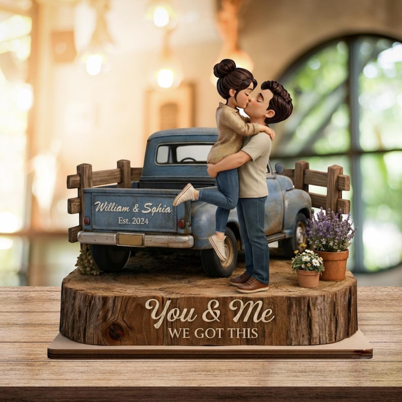 May include: A figurine of a couple kissing, standing in front of a blue pickup truck. The truck bed has the text "William & Sophia Est. 2024". The base reads "You & Me WE GOT THIS". The figurine is on a wooden base.