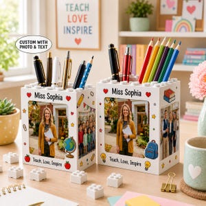 May include: Two white rectangular pencil holders featuring custom photo panels, the text "Miss Sophia" and "Teach, Love, Inspire," and colorful school-themed graphics including apples, globes, and backpacks, filled with various pens and pencils.