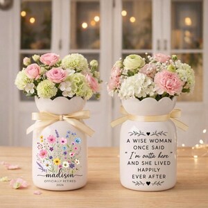 May include: Two white ceramic vases with floral arrangements. One vase has a floral design and the name "madison" with "OFFICIALLY RETIRED 2026". The other vase has the quote "A WISE WOMAN ONCE SAID 'I'm outta here' AND SHE LIVED HAPPILY EVER AFTER".