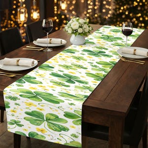 May include: A white table runner with a green shamrock and yellow flower pattern. The runner is placed on a dark brown wooden table set for a meal, with plates, silverware, and wine glasses.