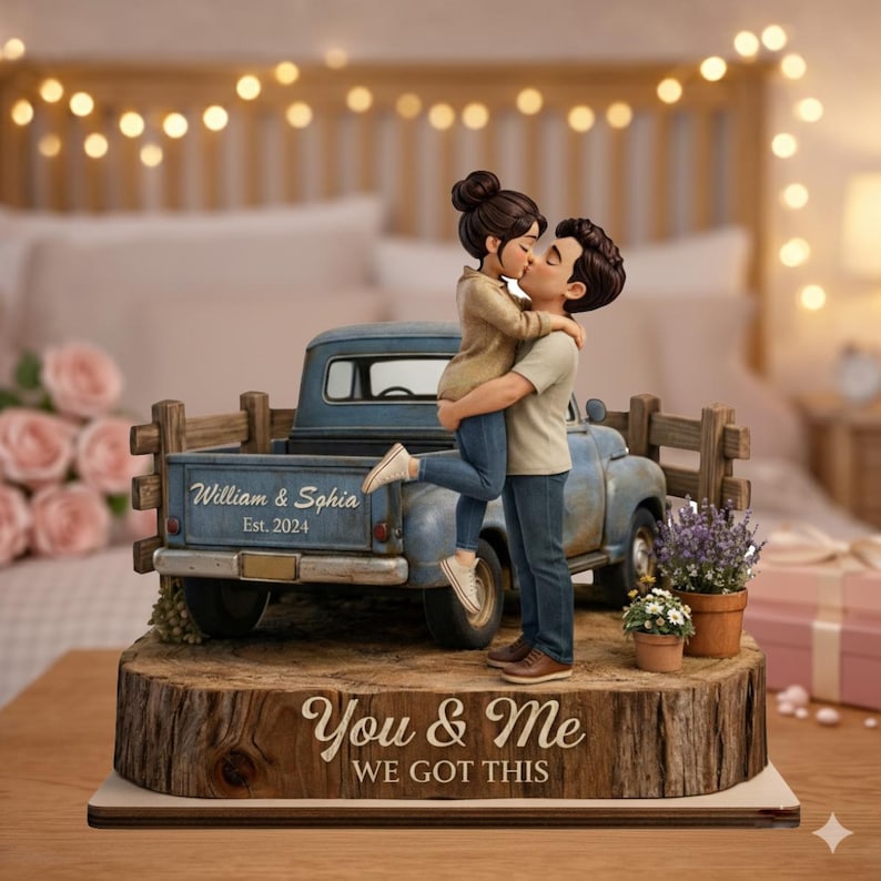 May include: A figurine of a couple kissing, standing in front of a blue pickup truck. The truck bed has the names "William & Sophia Est. 2024". The base reads "You & Me We Got This". The figurine is on a wooden base.