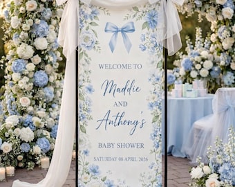 May include: A baby shower welcome sign with a floral design in shades of blue and white. The sign reads "Welcome to Maddie and Anthony's Baby Shower" with the date "Saturday 08 April 2026". The sign is decorated with a blue bow.