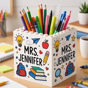 May include: A white square pencil holder constructed from interlocking building blocks. The exterior features colorful printed icons including light bulbs, apples, backpacks, and books, with the text "MRS. JENNIFER" printed on two sides.