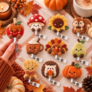 May include: A collection of ten felt badge reels featuring autumn-themed designs including a caramel apple, mushroom, sunflower, squirrel, hot cocoa, turkey, pear, wheat sheaf, hedgehog, and pumpkin, each with a smiling face and metal clip.