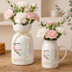 May include: Two white ceramic vases with floral arrangements. One vase is egg-shaped with a bow, the other is a pitcher. Both vases have the words "Grandma" and "Mom" with a heart design and names.