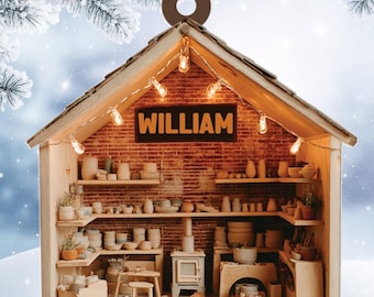 May include: A miniature wooden ornament shaped like a pottery studio, with shelves filled with ceramic pieces. The ornament features a brick wall backdrop, string lights, and the name "WILLIAM" on a sign. A festive holiday decoration.