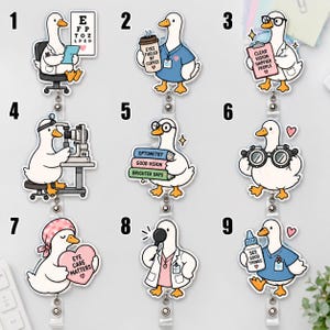 May include: A collection of nine badge reels featuring cartoon ducks in optometry-themed roles. Designs include ducks with eye charts, coffee cups, clipboards, medical equipment, books, glasses, heart-shaped signs, magnifying glasses, and eye drop bottles.
