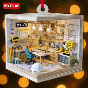 May include: A miniature diorama ornament depicting an architect's office, complete with a desk, blueprints, tools, and the name "WILLIAM". The ornament is made of wood and includes a red ribbon for hanging. The scene is illuminated by small lights.