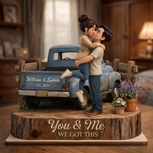 May include: A figurine of a couple kissing in front of a blue vintage truck. The truck bed has the names "William & Sophia" and "Est. 2024". The base reads "You & Me We Got This". The figurine is set on a wooden base with small potted plants.