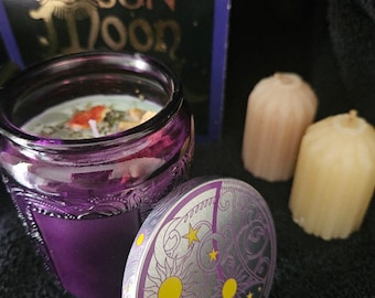 May include: Purple glass candle jar with a silver lid featuring a sun and moon design. The jar has a floral pattern and contains a green and white candle.