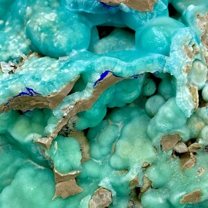 May include: Close-up of a mineral specimen with a vibrant turquoise hue. The surface has a bubbly, textured appearance with areas of brown and blue accents. The overall composition suggests a geological formation.