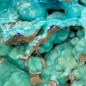 May include: Close-up of a mineral formation with a vibrant turquoise hue. The surface has a bubbly texture with areas of light brown and dark blue accents. The overall appearance is organic and crystalline.
