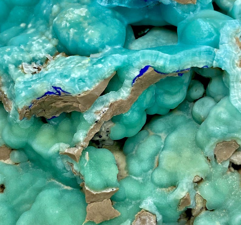 May include: Close-up of a mineral formation with a vibrant turquoise hue. The surface has a bubbly texture with areas of light brown and dark blue accents. The overall appearance is organic and crystalline.