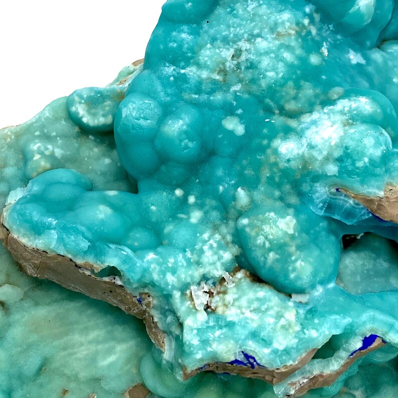 May include: Close-up of a vibrant, turquoise mineral formation. The surface is textured with rounded, bubbly formations and crystalline structures. The mineral has a mix of light and dark turquoise hues, with some areas of brown and white.
