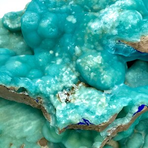 May include: Close-up of a mineral specimen featuring a vibrant turquoise hue with a bubbly texture. The mineral has a crystalline structure with areas of white and brown. The overall appearance is rough and natural, showcasing the beauty of geological formations.