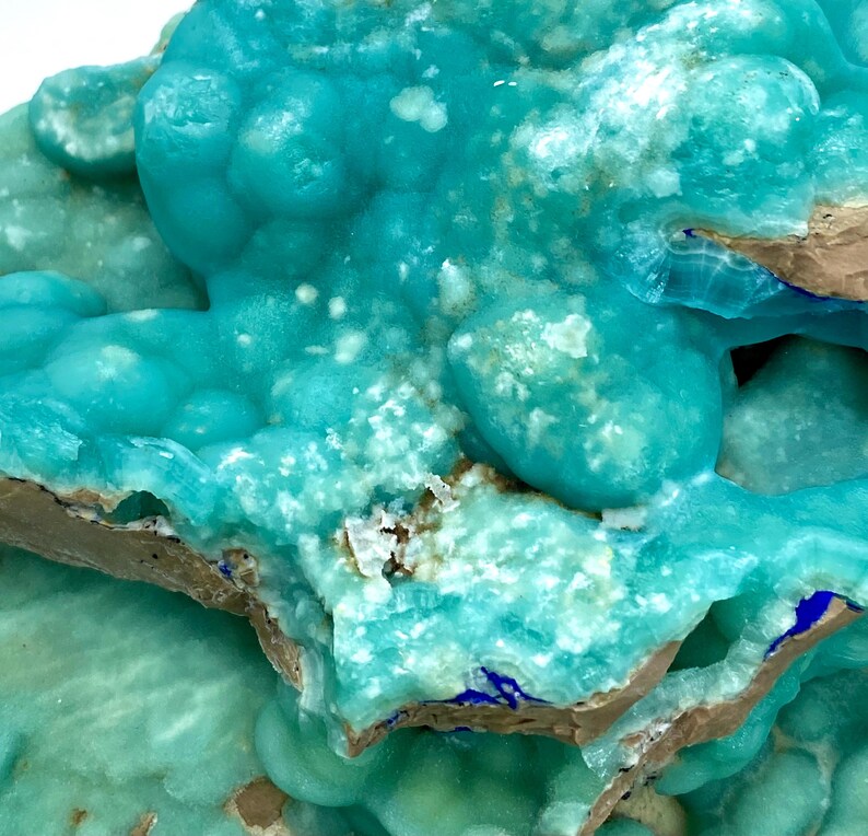 May include: Close-up of a mineral specimen featuring a vibrant turquoise hue with a bubbly texture. The mineral has a crystalline structure with areas of white and brown. The overall appearance is rough and natural, showcasing the beauty of geological formations.
